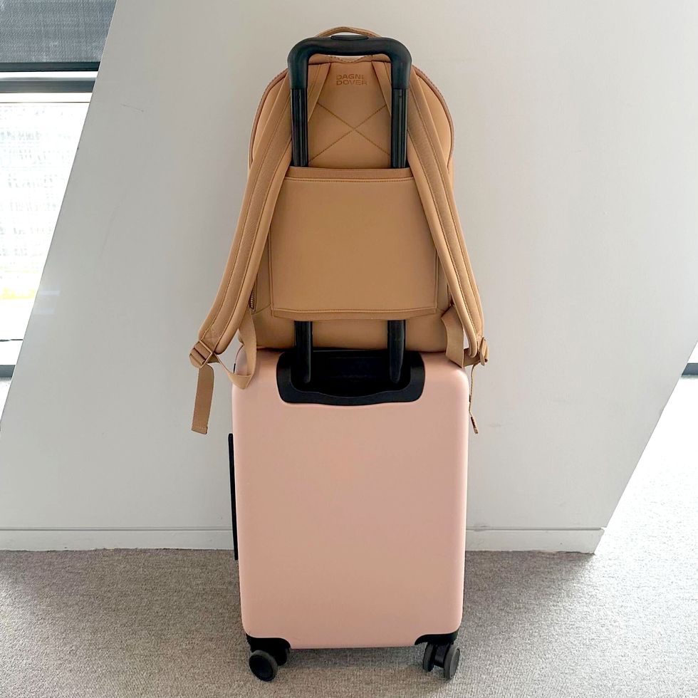 a tan backpack with a luggage sleeve on a pink carry on suitcase