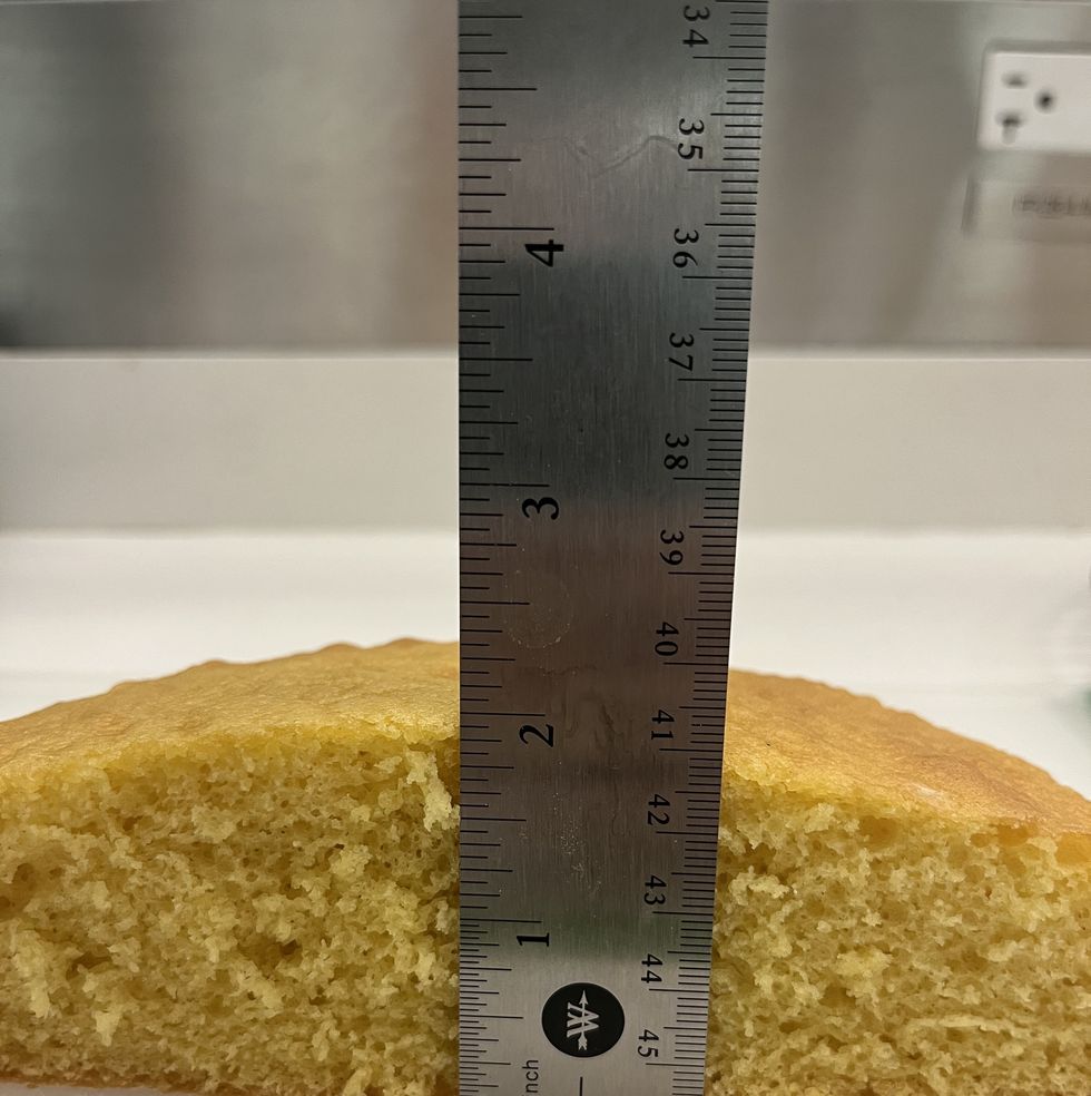 a yellow cake cut in half with a silver ruler measuring the height of the middle