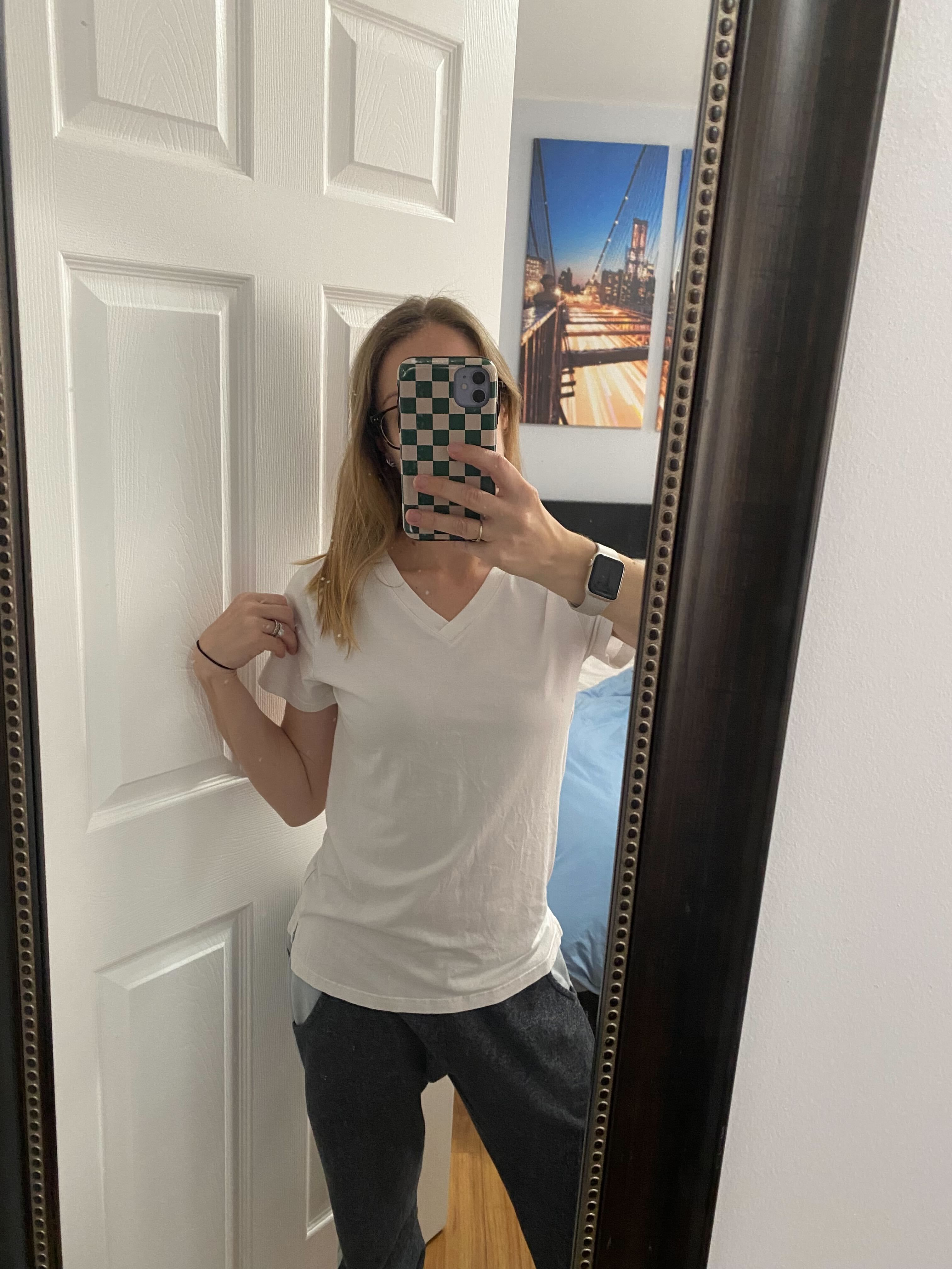a person poses in front of a mirror wearing a white vneck tshirt and gray sweatpants