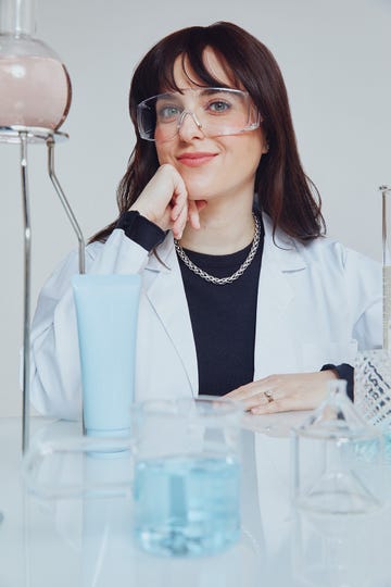 a laboratory setting featuring a woman in a lab coat surrounded by various glassware and liquids