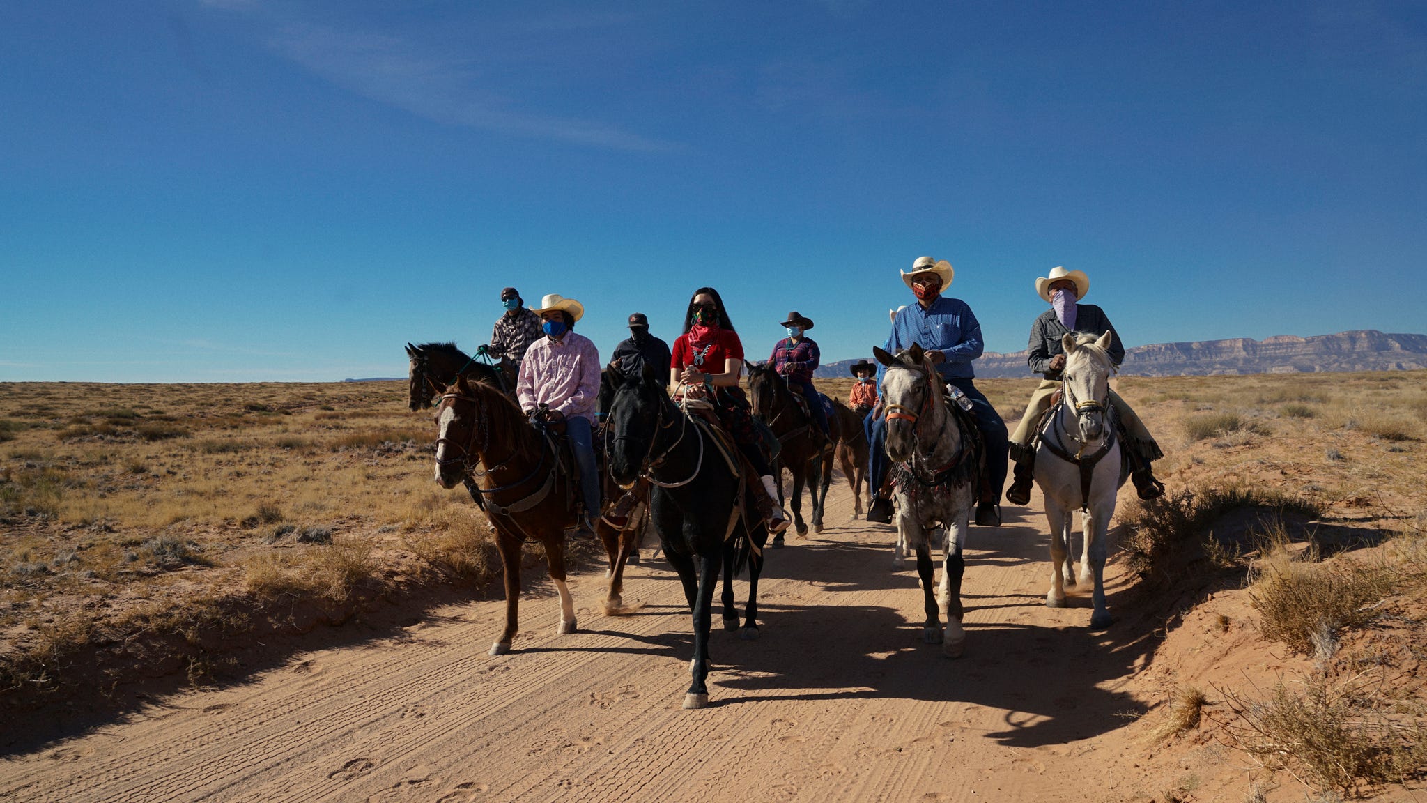 group of horseback riders on a dirt path in a desert landscape