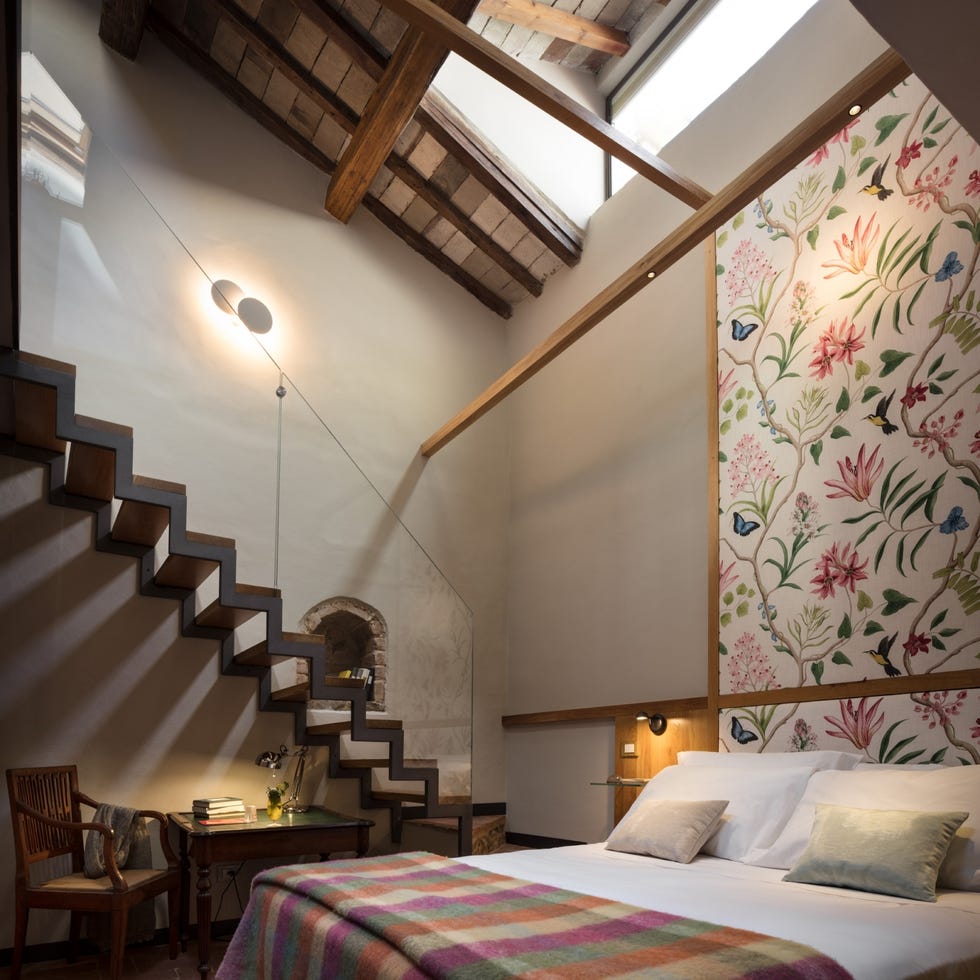 ottantotto hotel room interiors, with floral wallpaper behind bed, floating staircase, wall niche, desk, wooden beams, and more