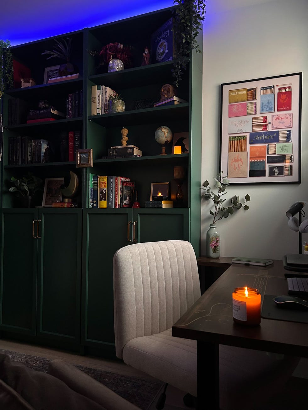 a cozy workspace featuring a green bookshelf a desk with a lit candle and decorative elements