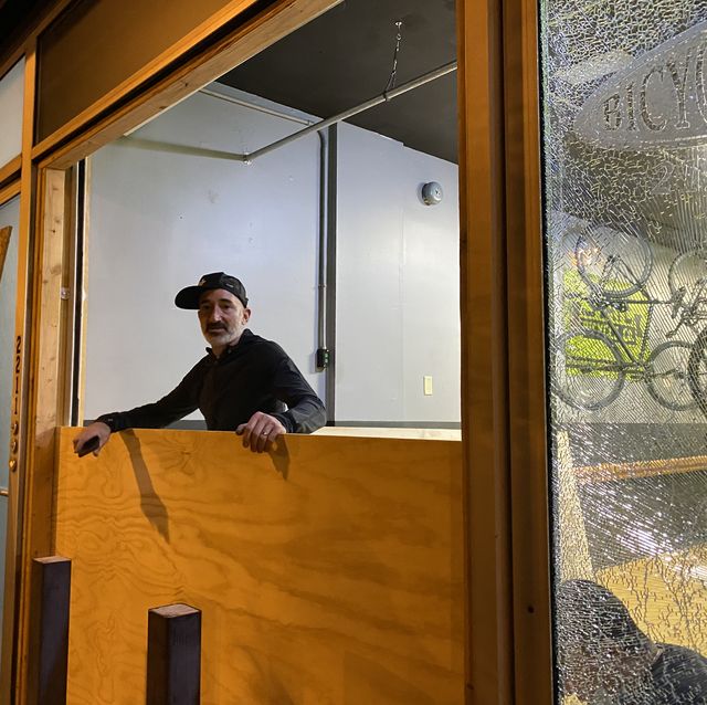 bicycle therapy owner lee rogers stands in the broken window of his storefront