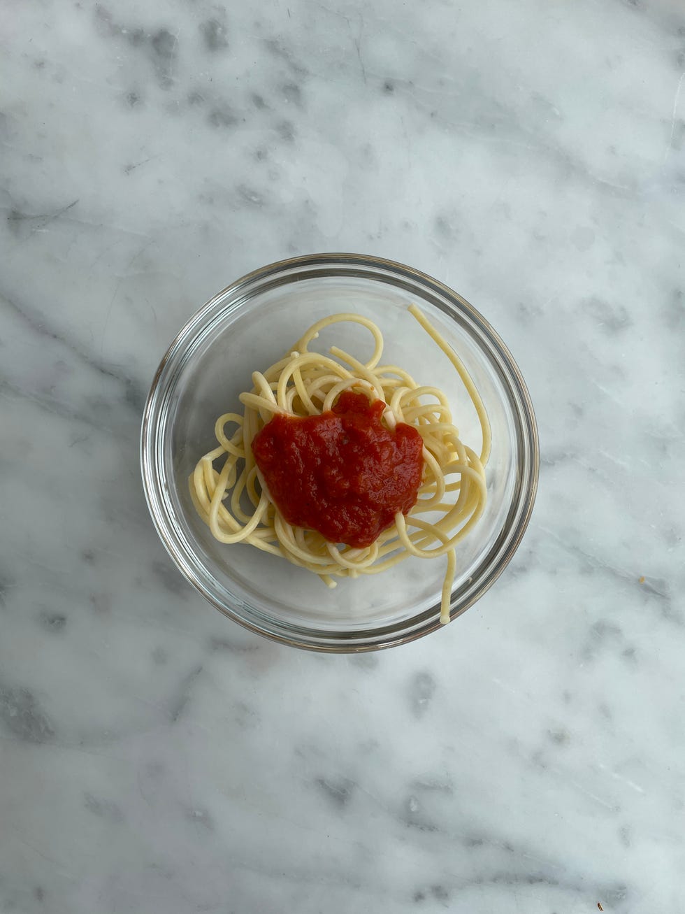a serving of spaghetti topped with tomato sauce in a glass bowl