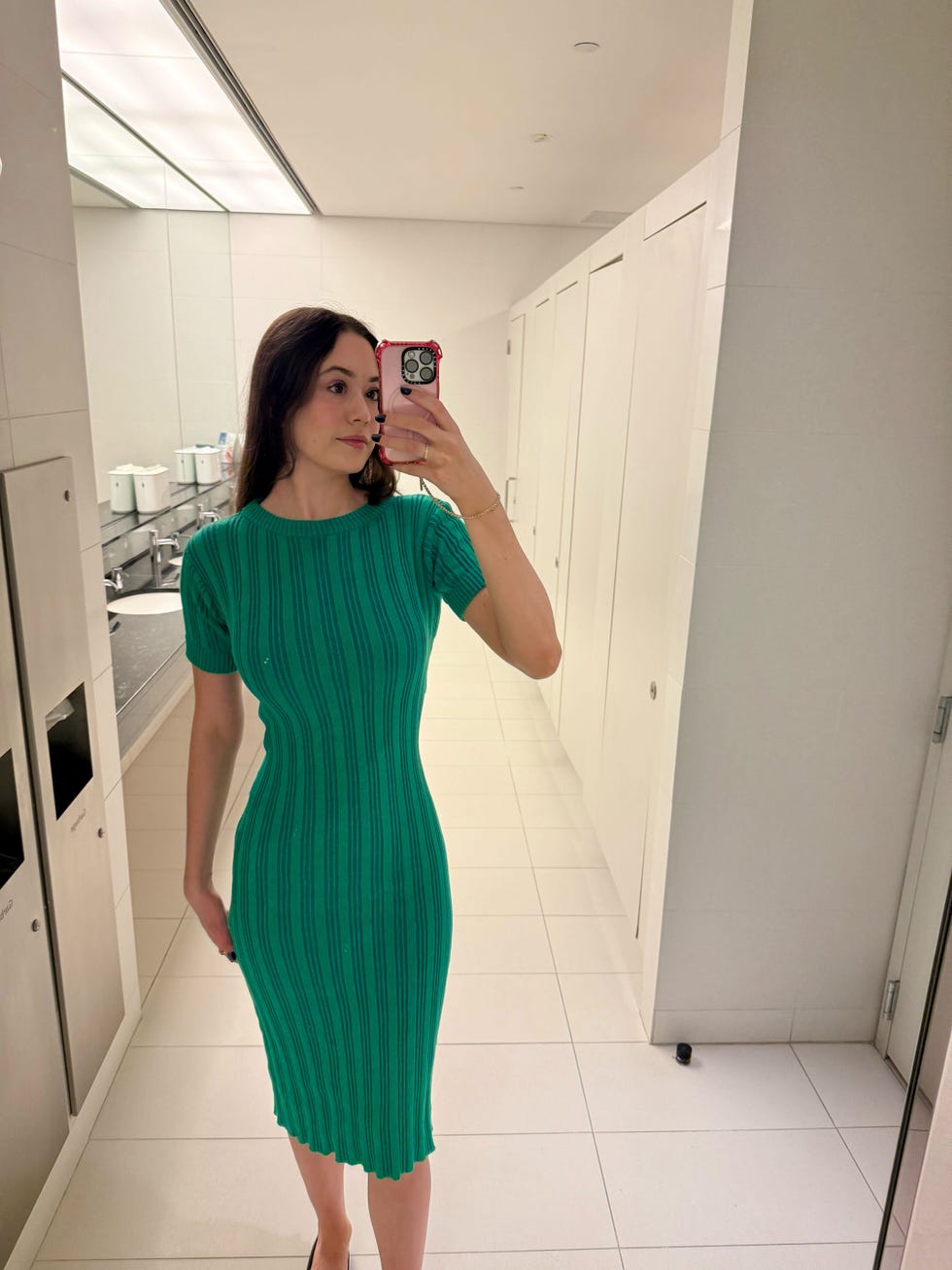 a reflection of a person wearing a green ribbed dress in a bathroom