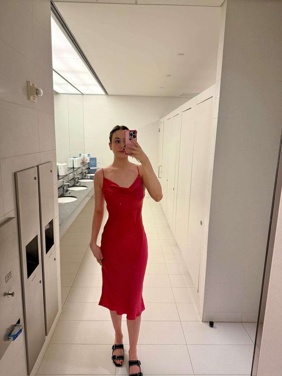 woman standing in a bathroom wearing a red dress and black sandals