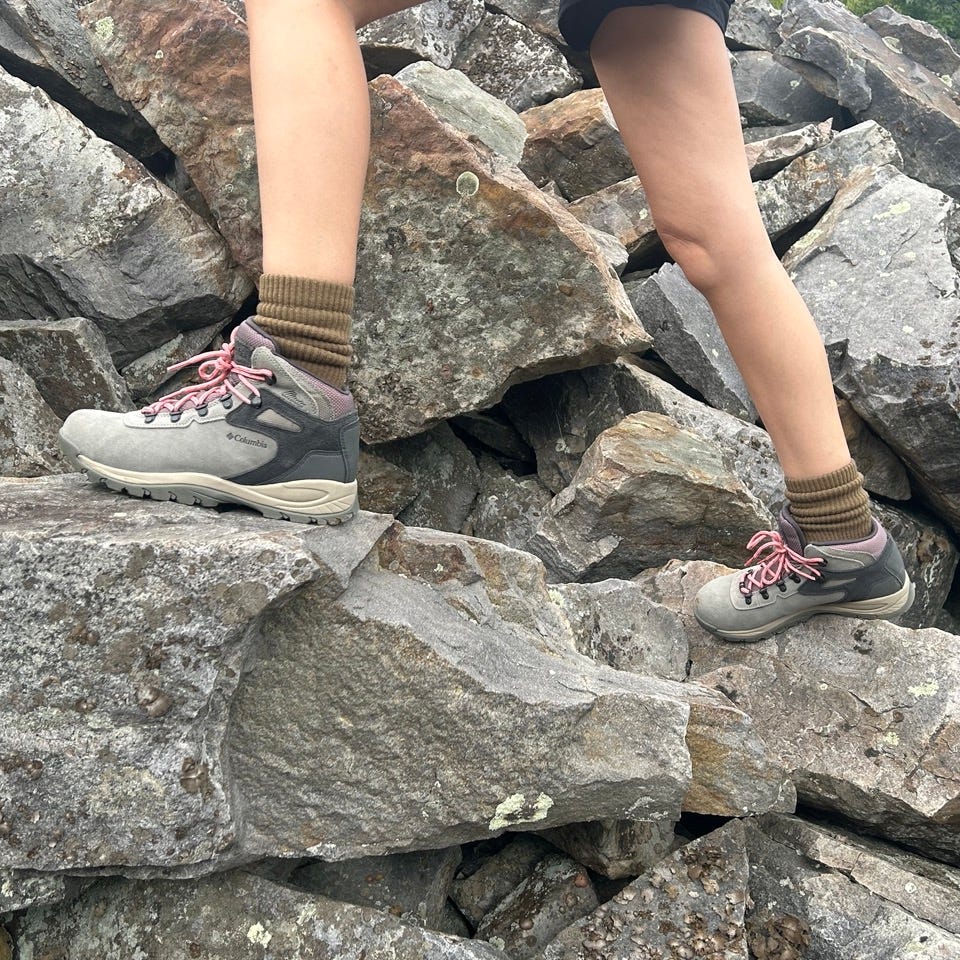 best hiking boots - how we test consumer pic a person wearing gray hiking boots with brown crew socks climbs technical rocky terrain