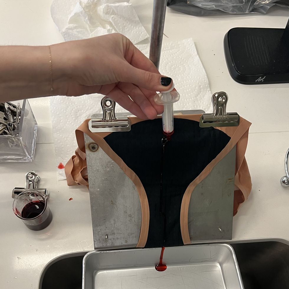 a gh analyst putting red cough syrup on a pair of period underwear at a 45 degree angle as part of good housekeeping's best period underwear testing