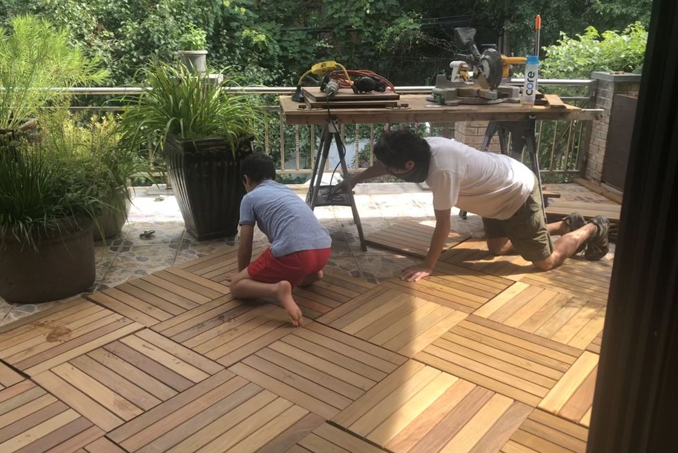 a man and child lay wooden deck tiles during the renovation of a back terrace