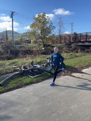 a jogger is running on a paved path beside a grassy area with discarded materials such as metal and tires scattered nearby