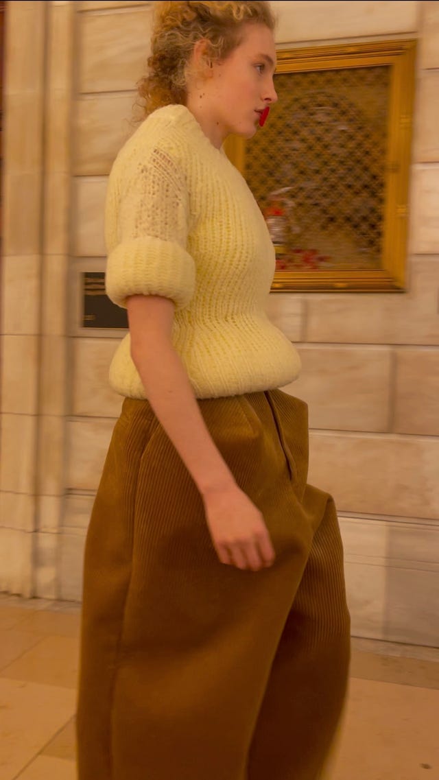individual walking while wearing a white sweater and brown pants