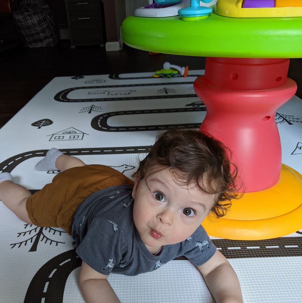 a baby lays on a play at while holding two toys, part of a good housekeeping story on the best baby play mats