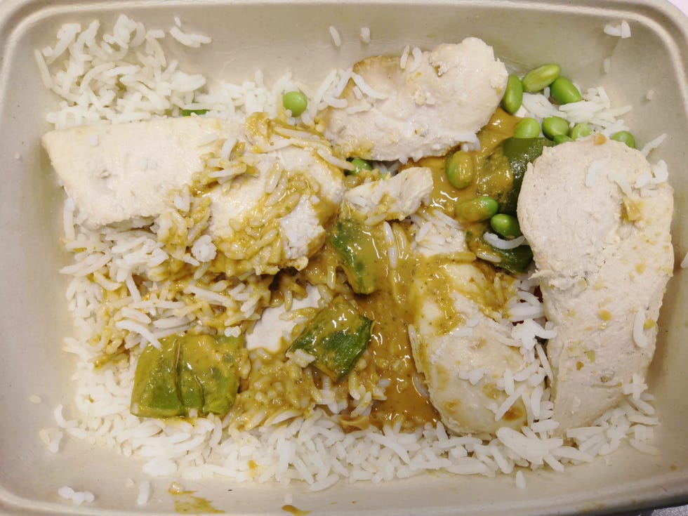 container of rice topped with chicken and green vegetables in sauce