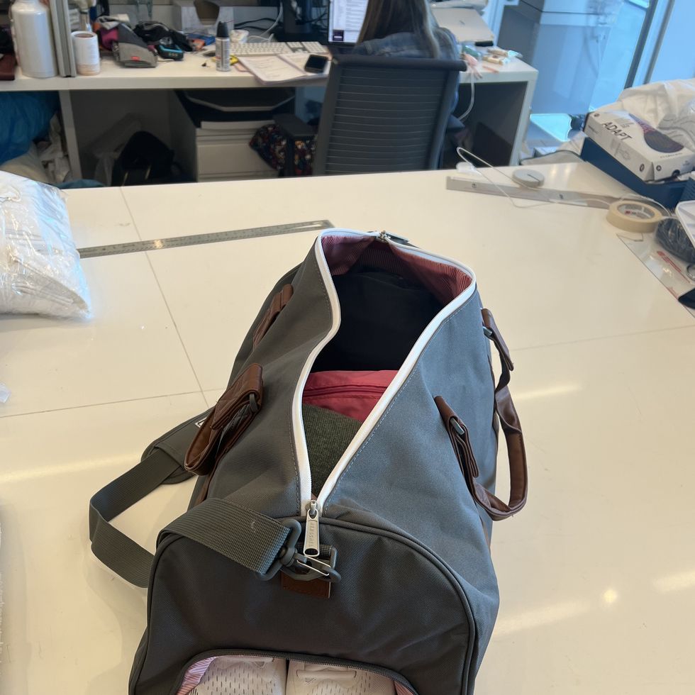 a grey duffel on a white table filled with clothes and sneakers as part of good housekeeping's testing to find the best duffels