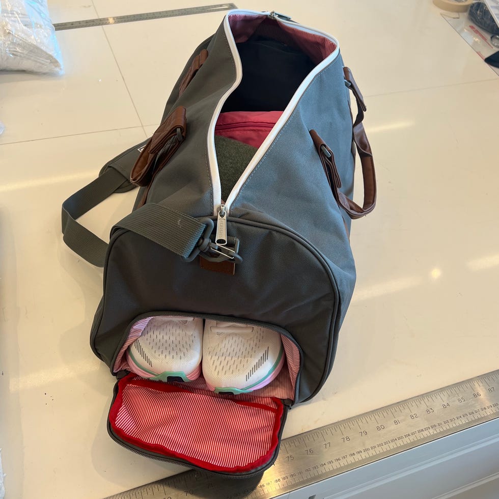 a grey duffel on a white table filled with clothes and sneakers as part of good housekeeping's testing to find the best duffels