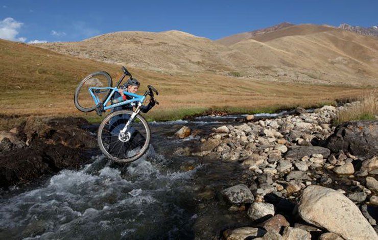 shannon galpin crossing a river with her bike