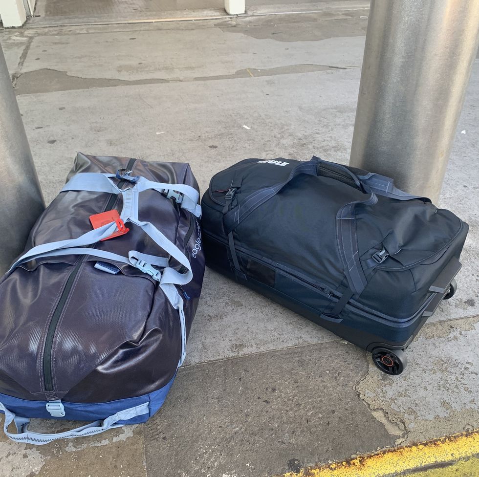 two navy duffels on a curb outside an airport as part of good housekeeping's testing for the best duffels