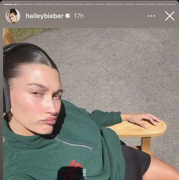 hailey bieber takes a selfie while sitting outside on a bench