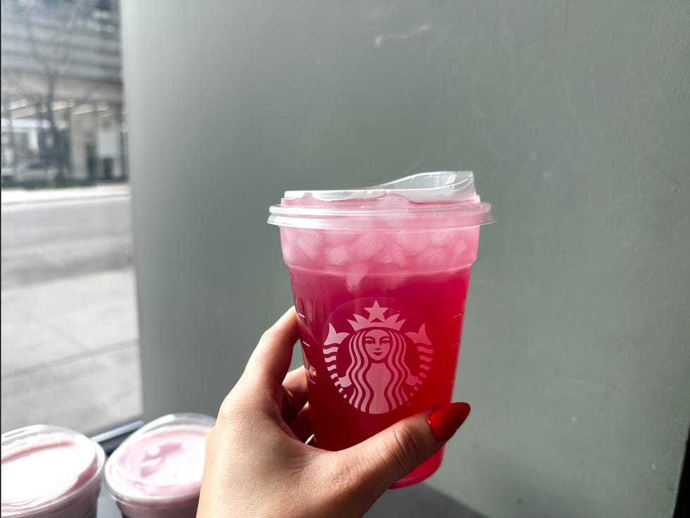 a hand holding a beverage cup with a pink drink from starbucks