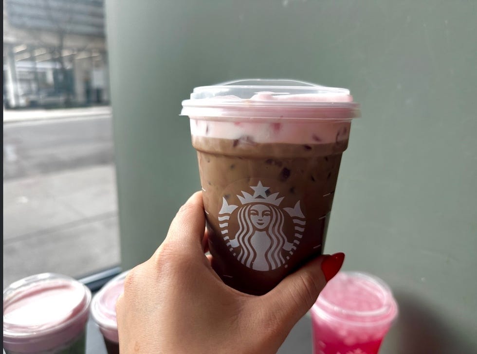 iced coffee drink with whipped cream and pink topping held by a person