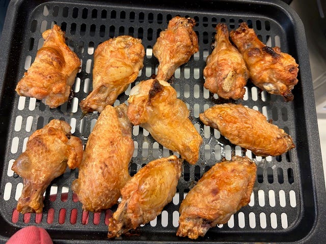 a tray containing a dozen cooked chicken wings, arranged with some overlapping the wings have a crispy golden brown exterior and appear juicy, suggesting they have been recently cooked the tray features a grid design allowing for drainage of grease