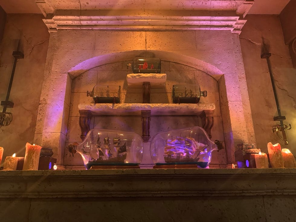 shelf displaying intricately crafted ship models inside glass bottles surrounded by candles