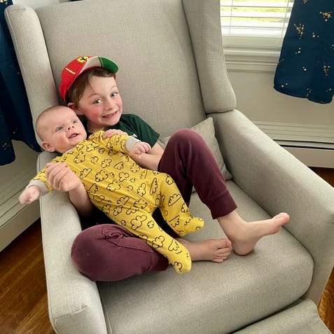 testing a nursery glider for good housekeeping a boy holds his baby brother on a nursery glider