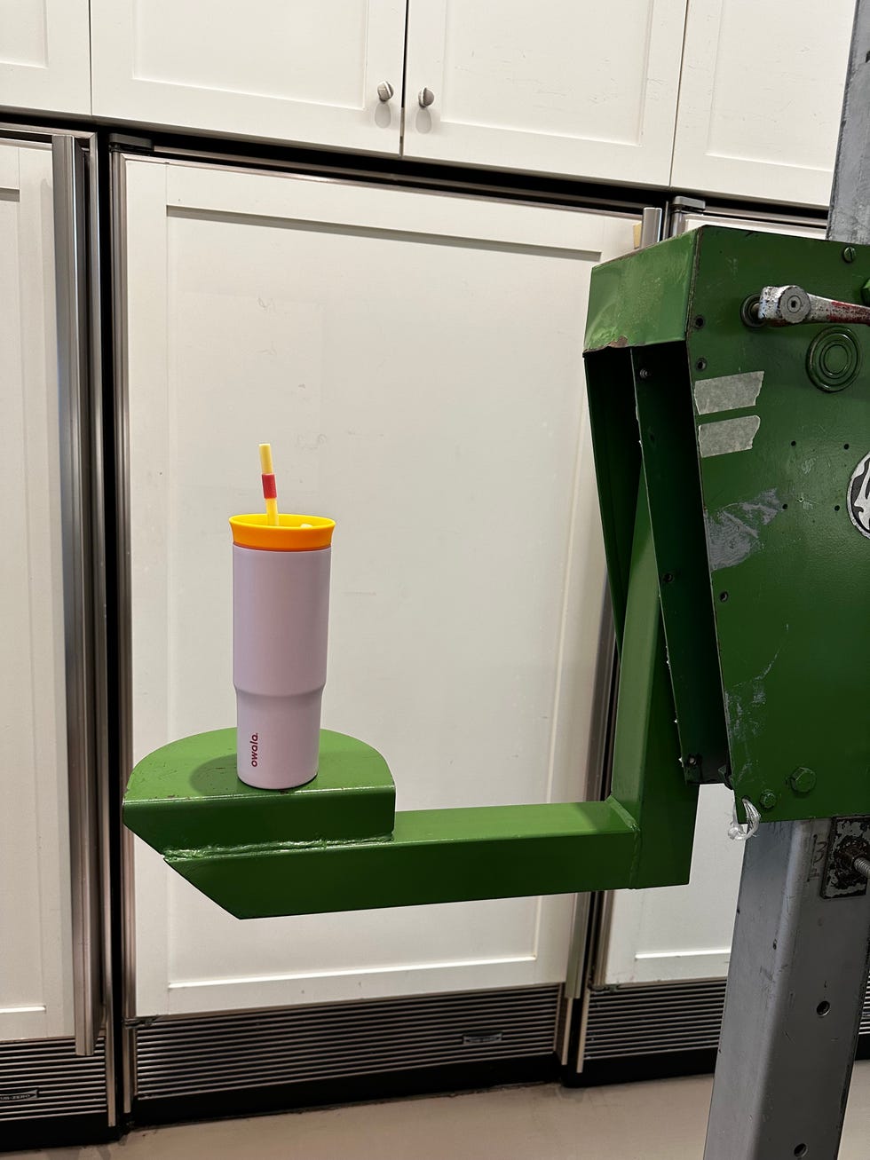 a pink tumbler with a yellow lid and straw placed on a green platform against a kitchen backdrop