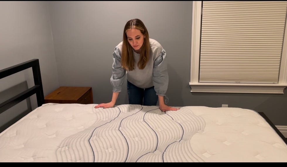 person touching and looking at a mattress on a bedframe