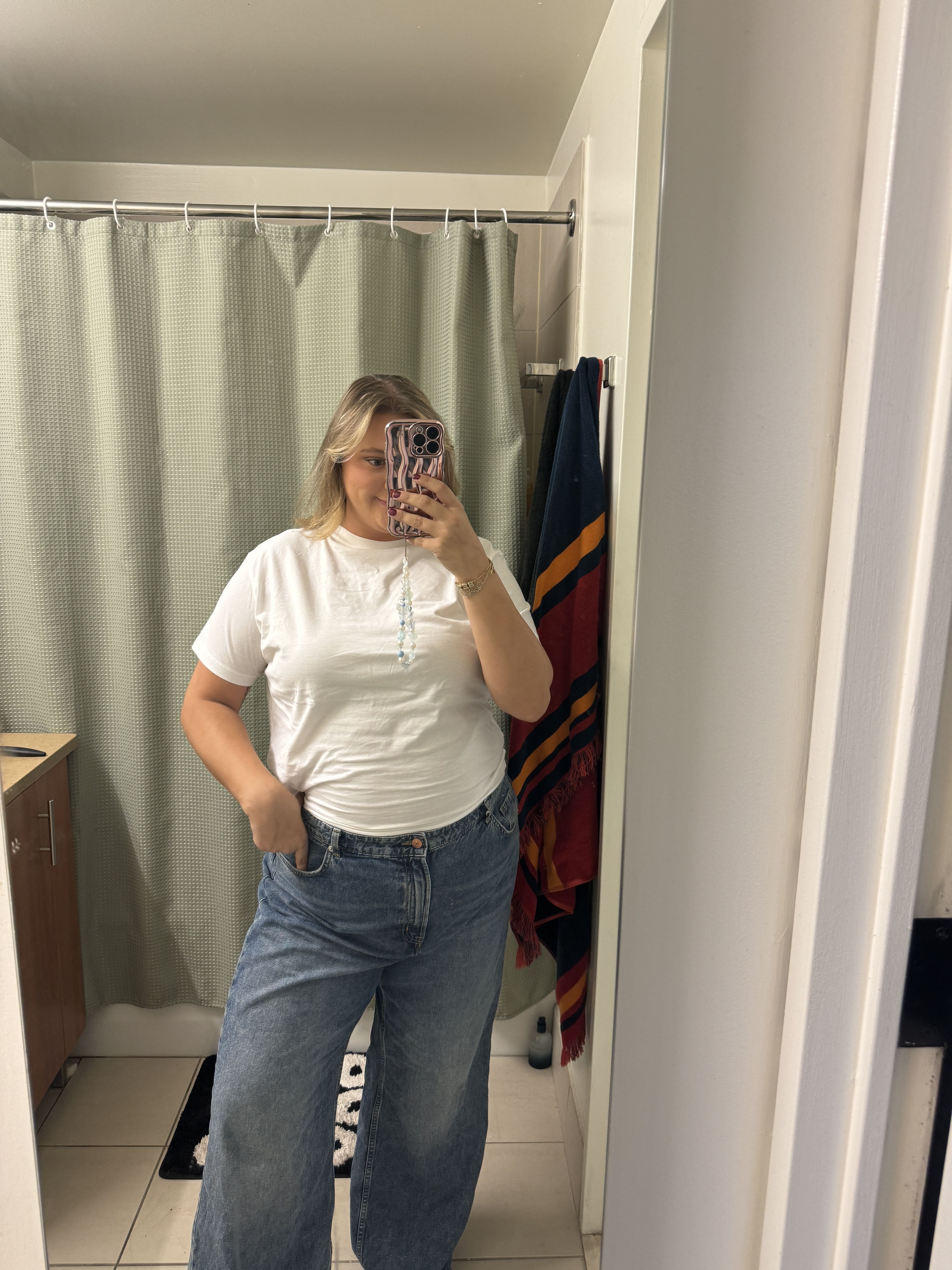 person standing in a bathroom mirror wearing a white shirt and blue jeans
