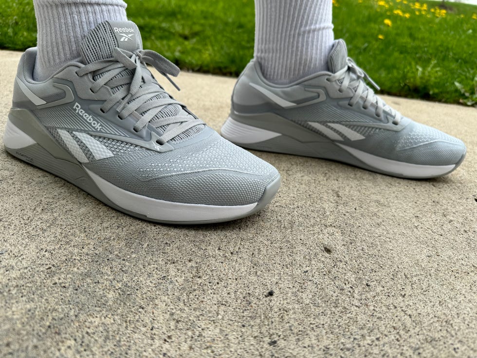 a tester wearing a pair of grey reebok nano x4 sneakers outside on the sidewalk as part of good housekeeping's testing for the best cross training shoes