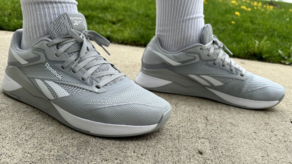 a tester wearing a pair of grey reebok nano x4 sneakers outside on the sidewalk as part of good housekeeping's testing for the best walking shoes for men