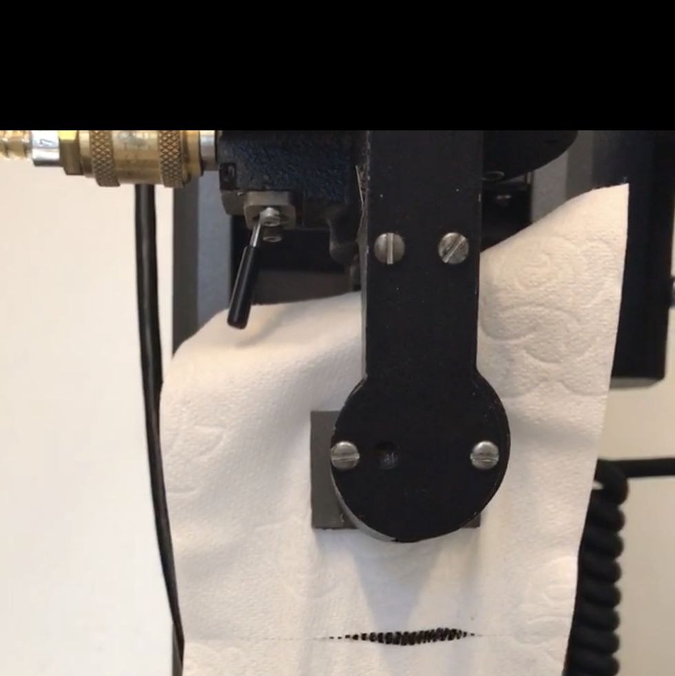 toilet paper is placed between the two clamps on the instron machine, which is pulling the toilet paper apart to measure perforation strength