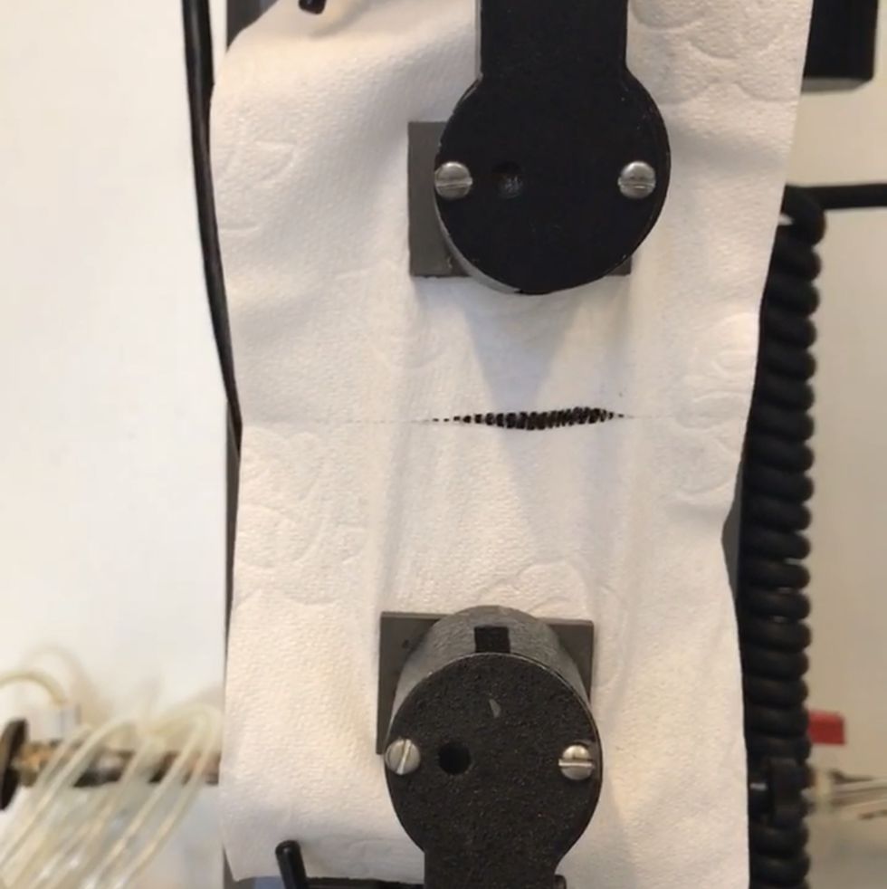 toilet paper is placed between the two clamps on the instron machine, which is pulling the toilet paper apart to measure perforation strength