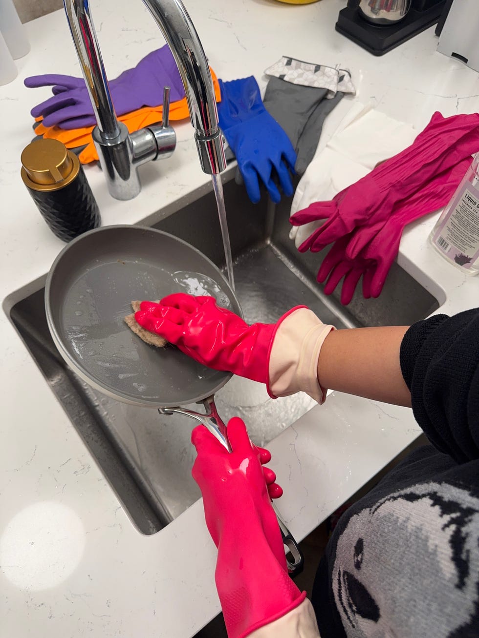 person washing a pan wearing a pair of pink dishwashing gloves