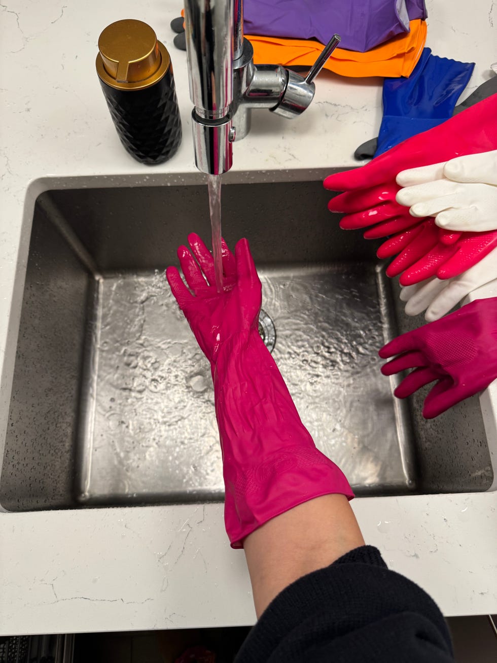 hands wearing pink dishwashing gloves under running water in a sink