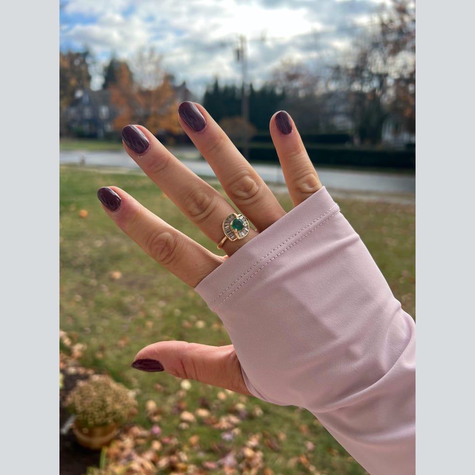 outstretched hand displaying manicured nails and a ring with a blurred outdoor background
