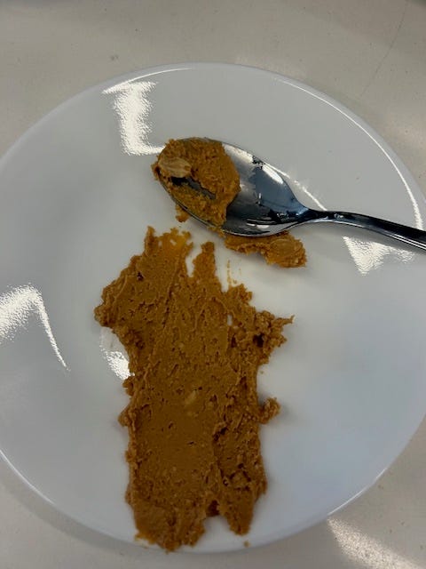 peanut butter smeared on a white plate with a spoon on the side