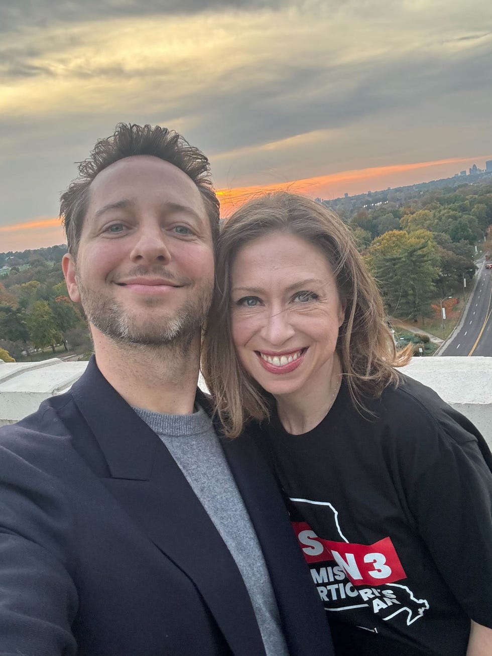 two individuals pose for a selfie with a scenic sunset background