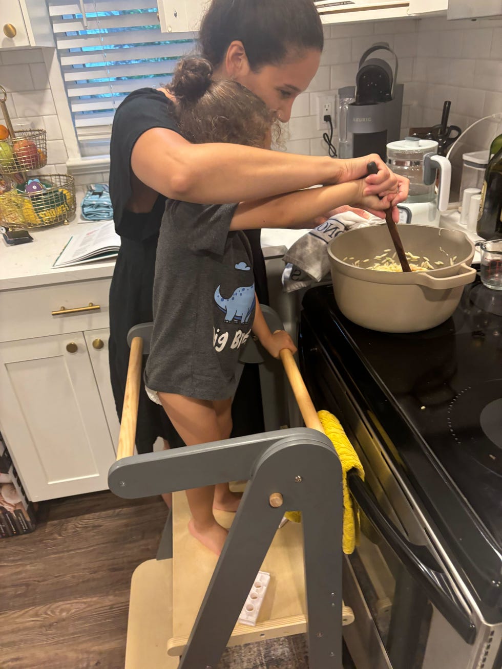 a mom helps her child stir while he stands on a learning tower