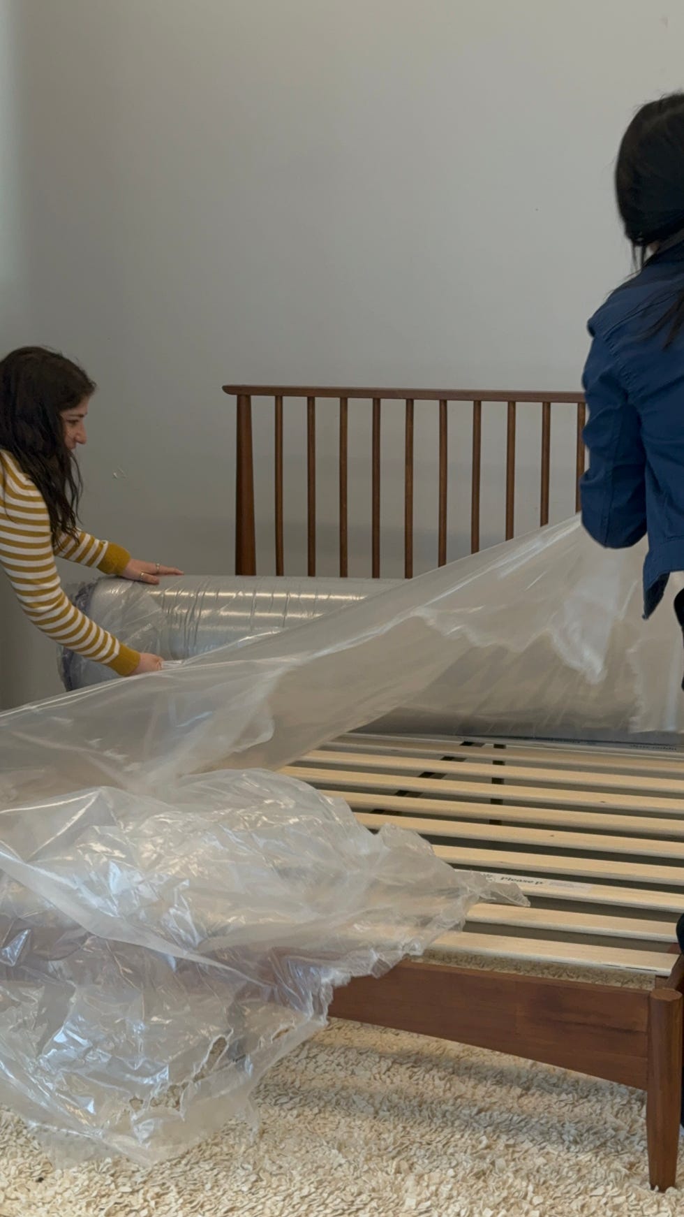 two people removing plastic from a rolled up purple mattress