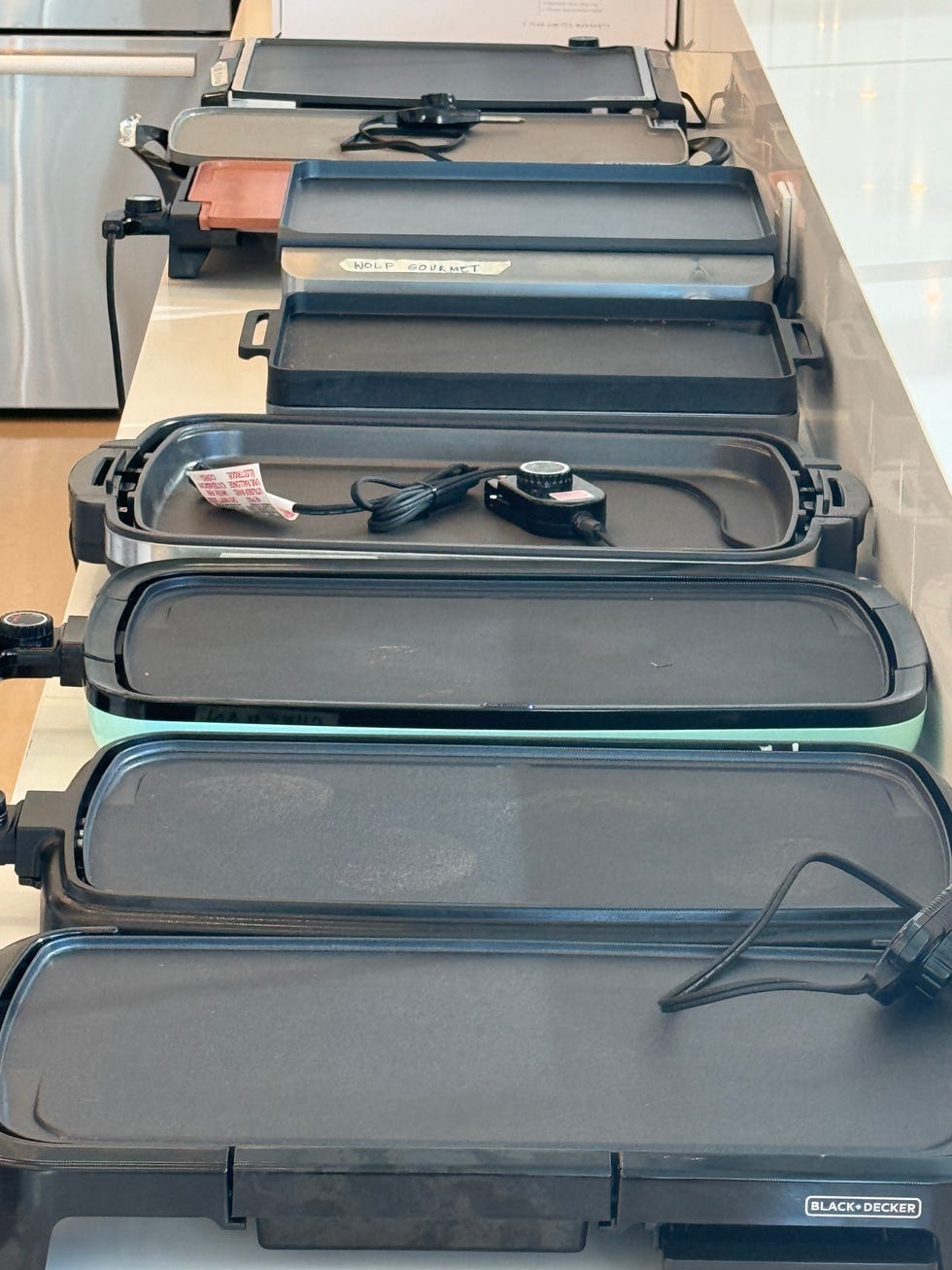 a lineup of electric griddles of different brands positioned on a countertop