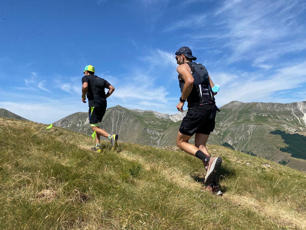 runners ascending a grassy hill in a mountainous region