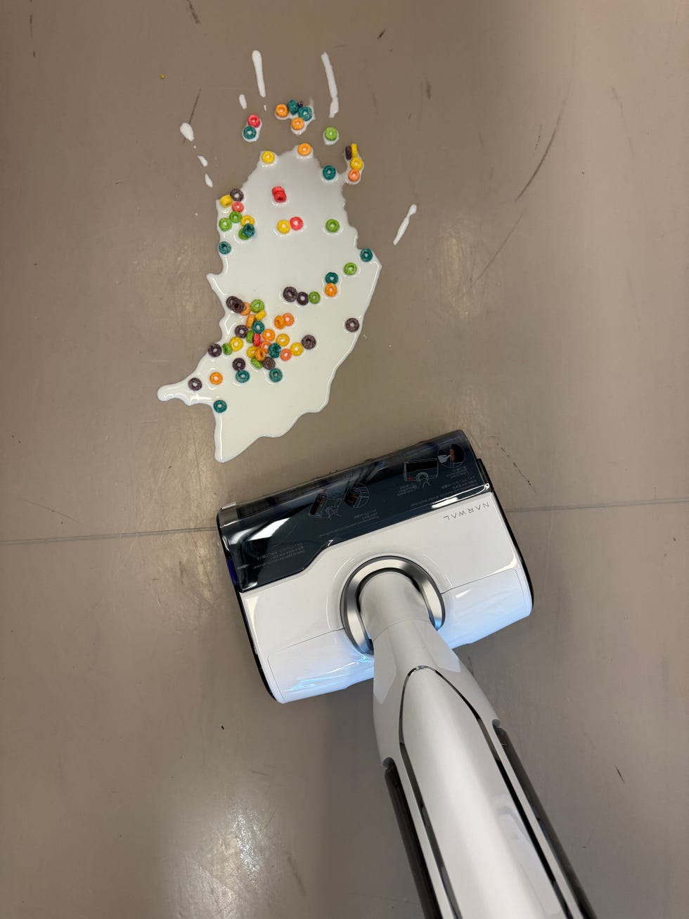 a vacuum mop is cleaning a spilled mixture of colorful cereal and milk on the floor