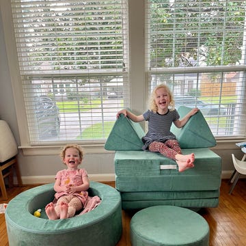 sisters test the nugget play couch and chunk ottoman two children play with green modular seating furniture the nugget play couch and the chunk ottoman