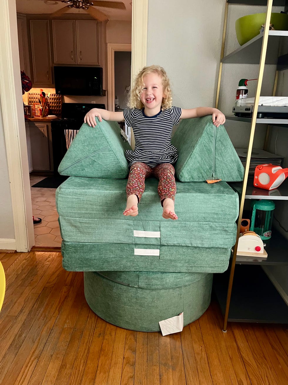 a child sits atop seafoam green play furniture from the brand nugget, including their couch and ottoman