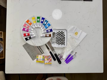 various cake decorating tools such as food color, piping tips, spatulas and piping bags on a marble counter
