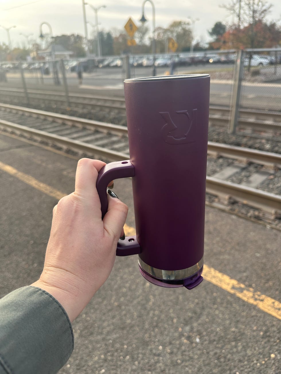 a person holding a purple travel mug near train tracks