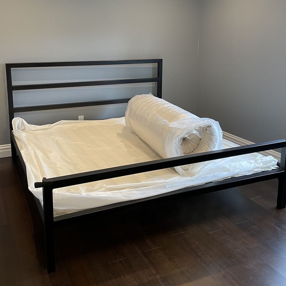 a black metal bed frame with a white packaged mattress on top